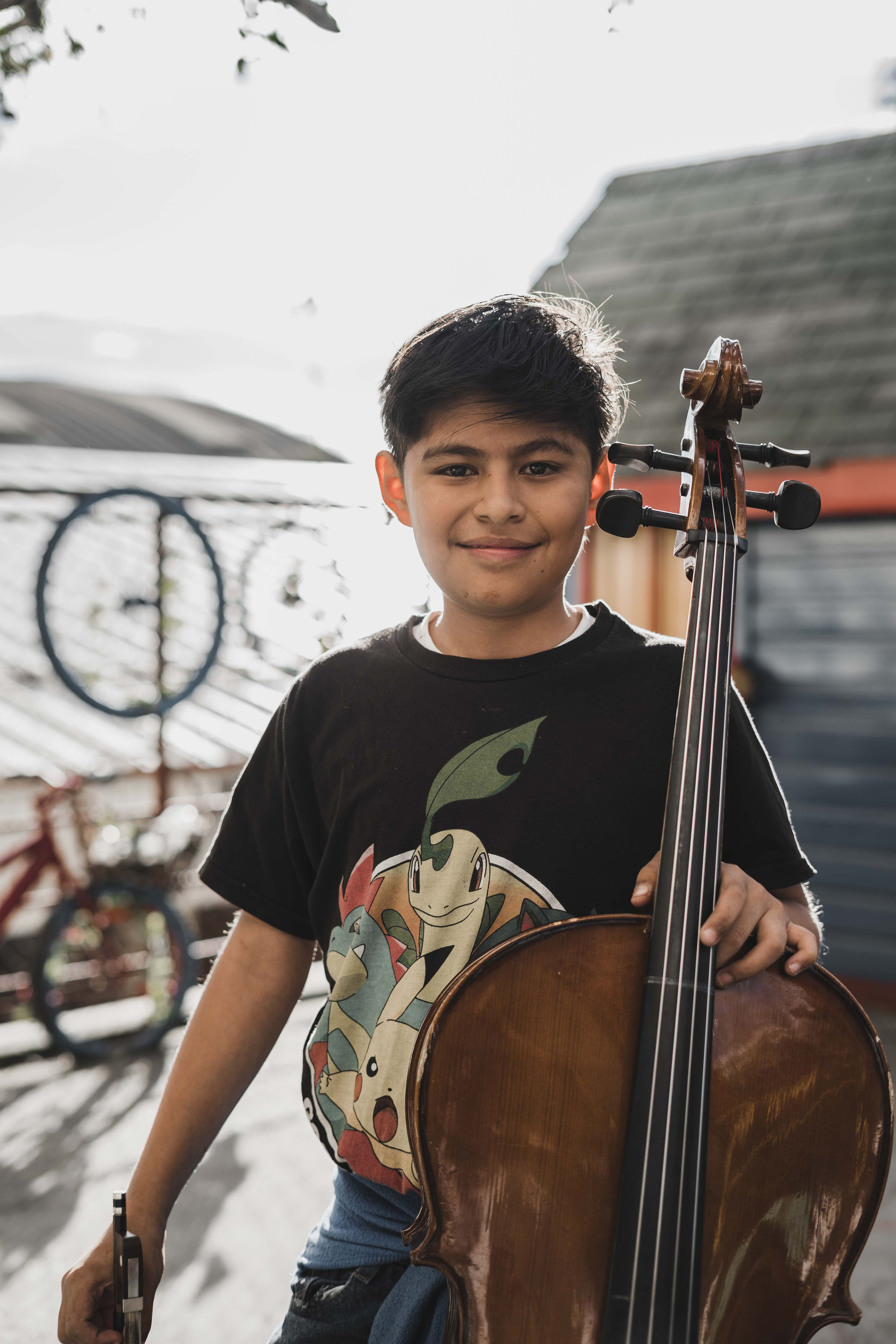 A young cellist smiling, holding his instrument